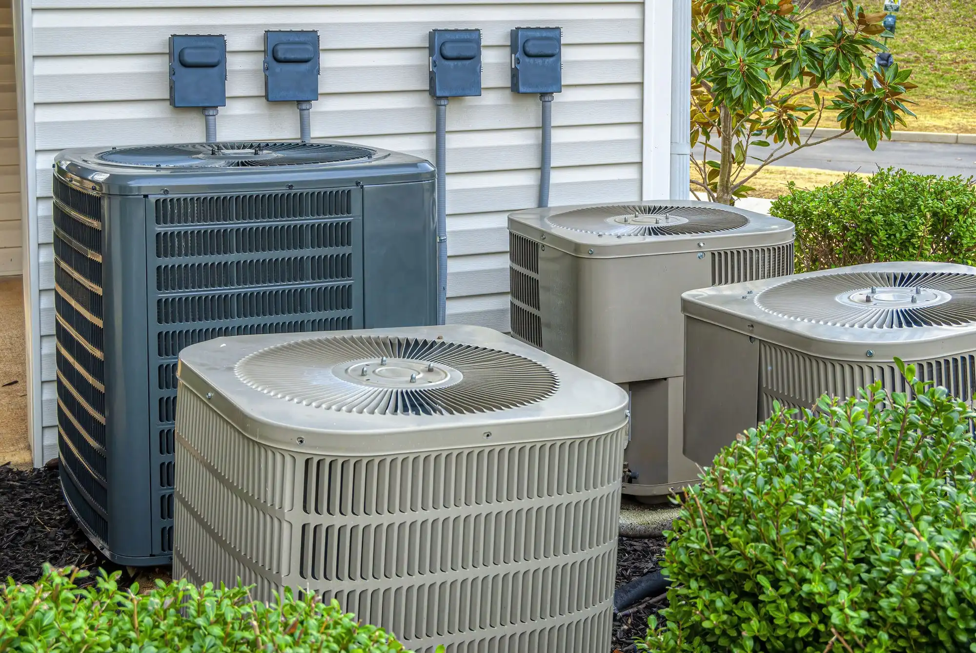 Four air conditioning condenser units beside a house, each with its own disconnect box