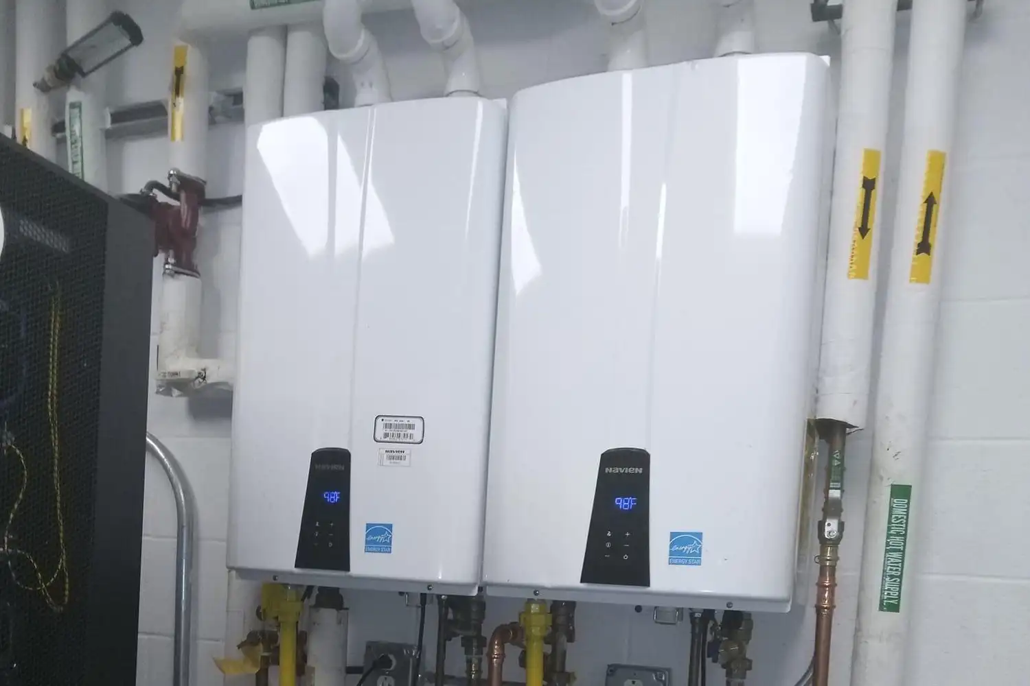 Two wall-mounted tankless water heaters with copper and gas piping in a mechanical room